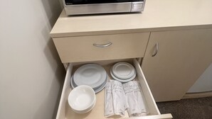 A microwave on a cabinet with a drawer containing plates, bowls, and napkins. - Overlander Motor Lodge (Gunnedah)