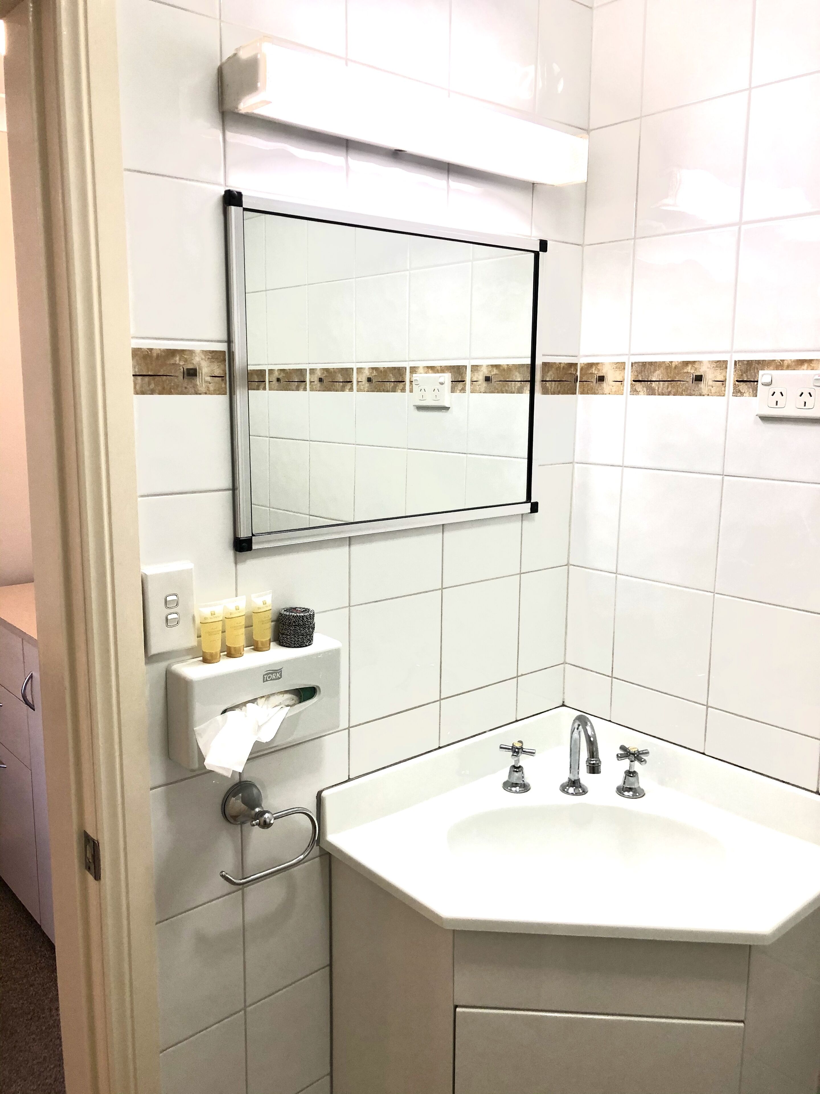 A bathroom with a white sink, a mirror, and a towel dispenser.
