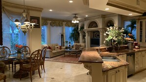 A spacious kitchen with a large island, a dining area with a glass table, and a living room with a sofa and decorative plants.