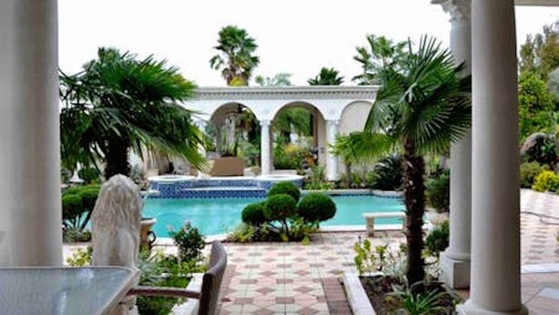 A pool area with a tiled walkway, palm trees, and a fountain.