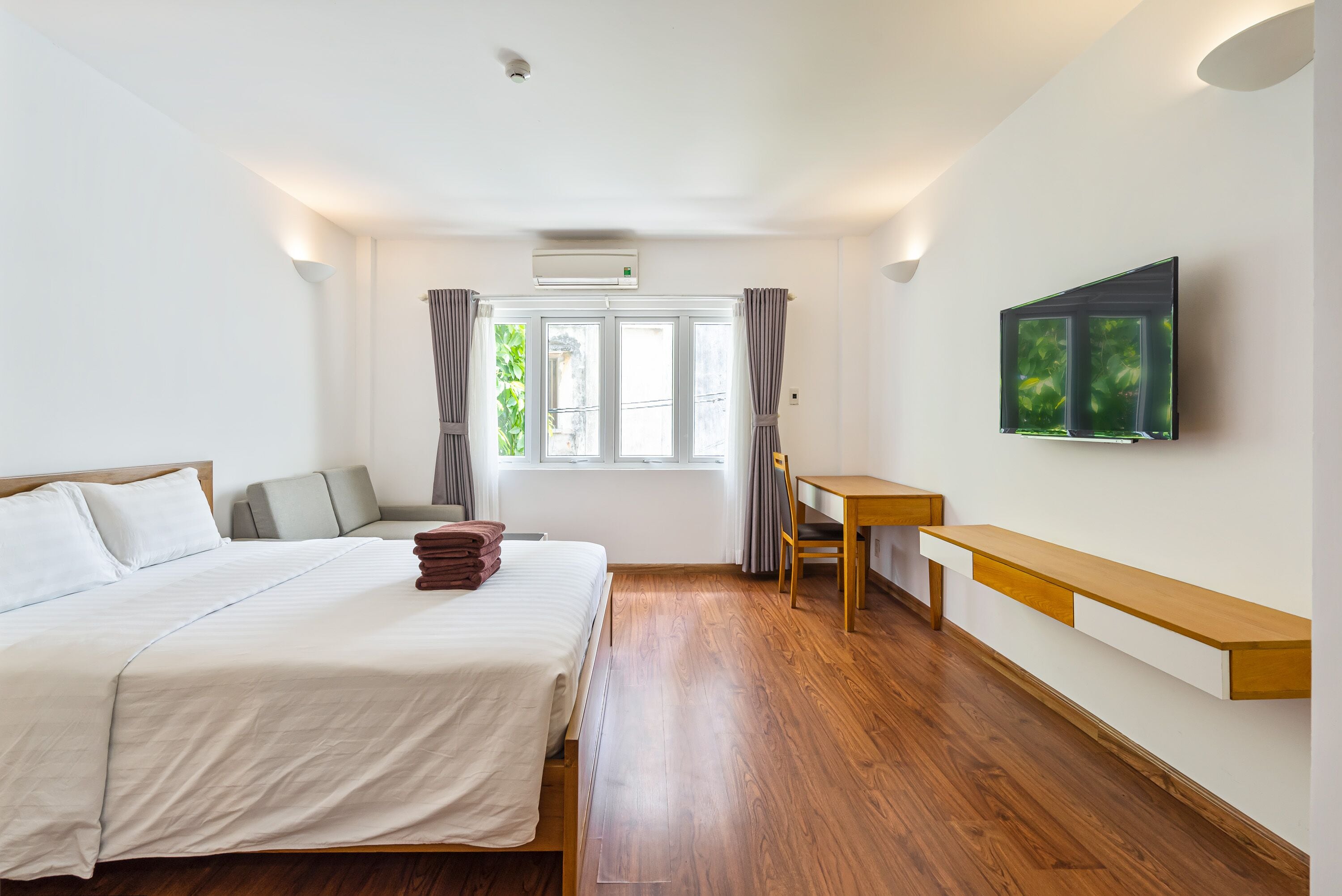 A bedroom with a bed, a desk, a chair, a TV, and a window with curtains.
