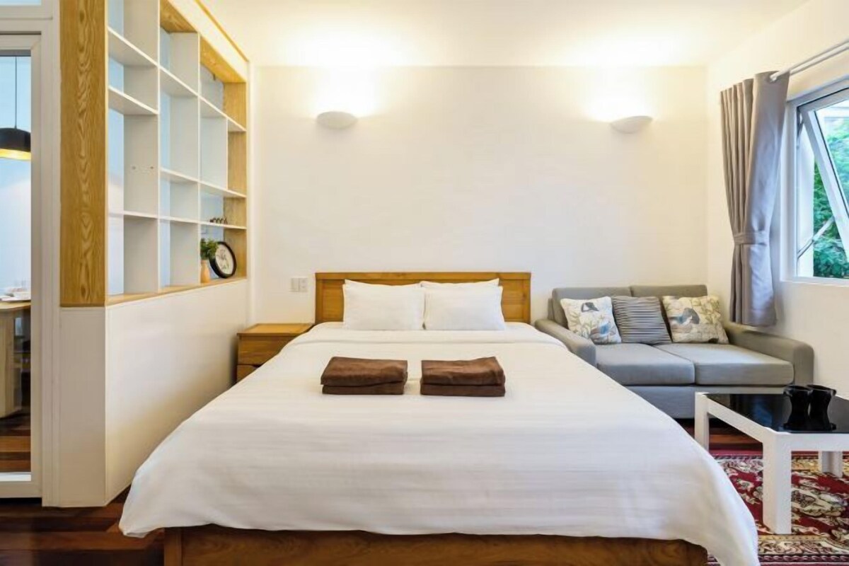 Una habitación de hotel con una cama grande, un sofá, una mesita y una ventana con cortinas.