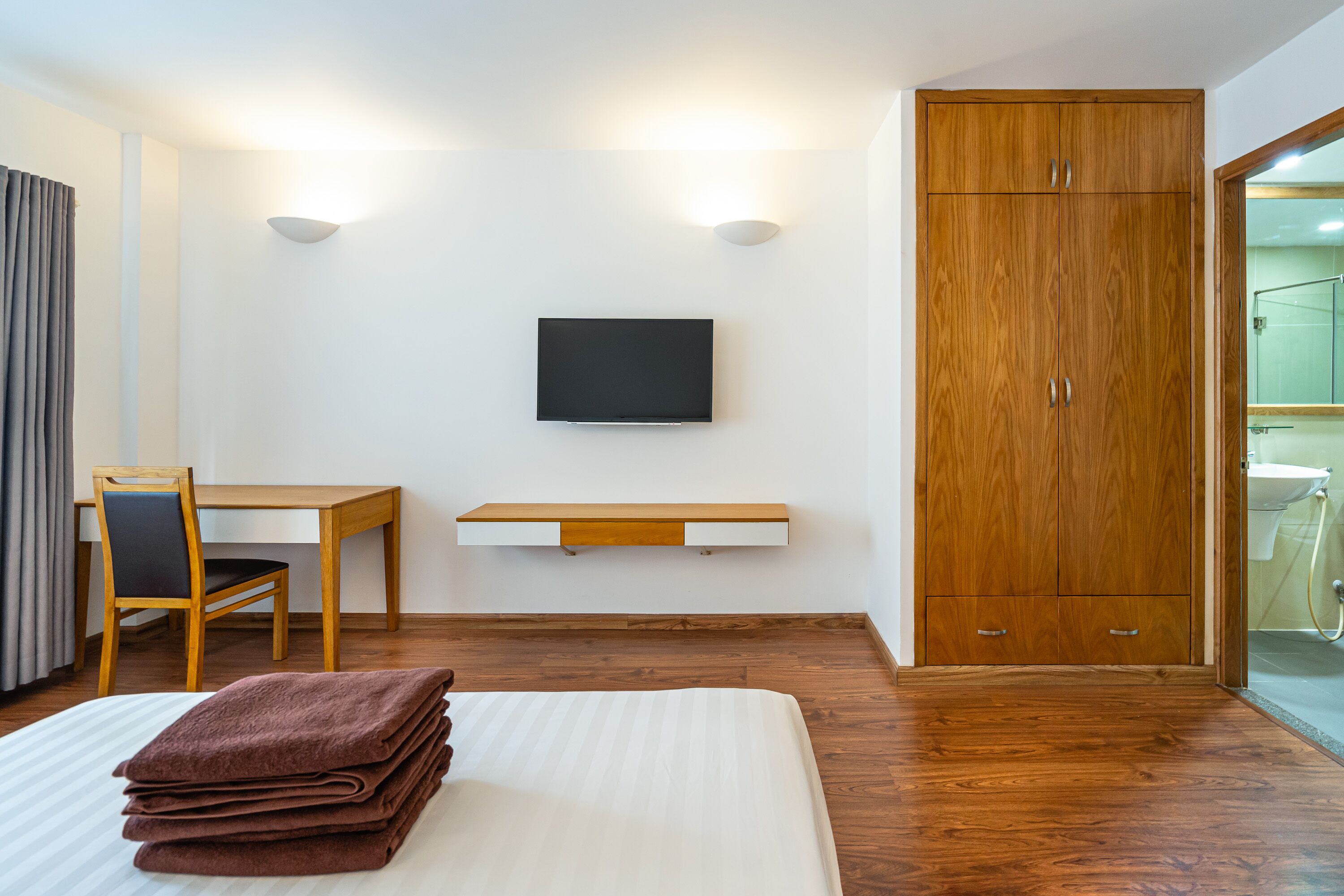 Et hotelværelse med en seng, et skrivebord med stol, et tv ophængt på væggen og et klædeskab.