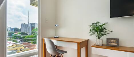 Una habitación moderna con un escritorio de madera, una silla gris, una planta en maceta y un televisor en la pared.