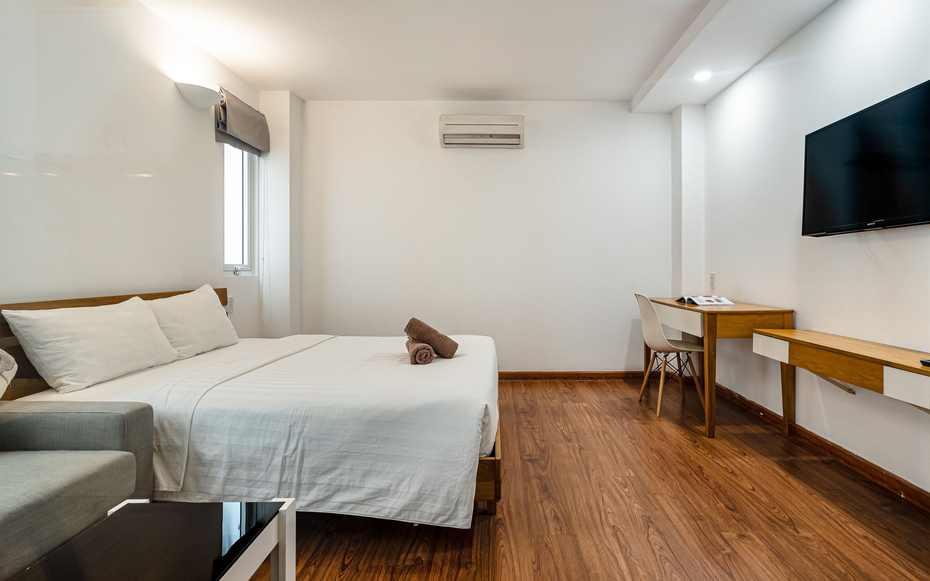 Een hotelkamer met een bed, een bureau, een stoel, een televisie en een airconditioning.
