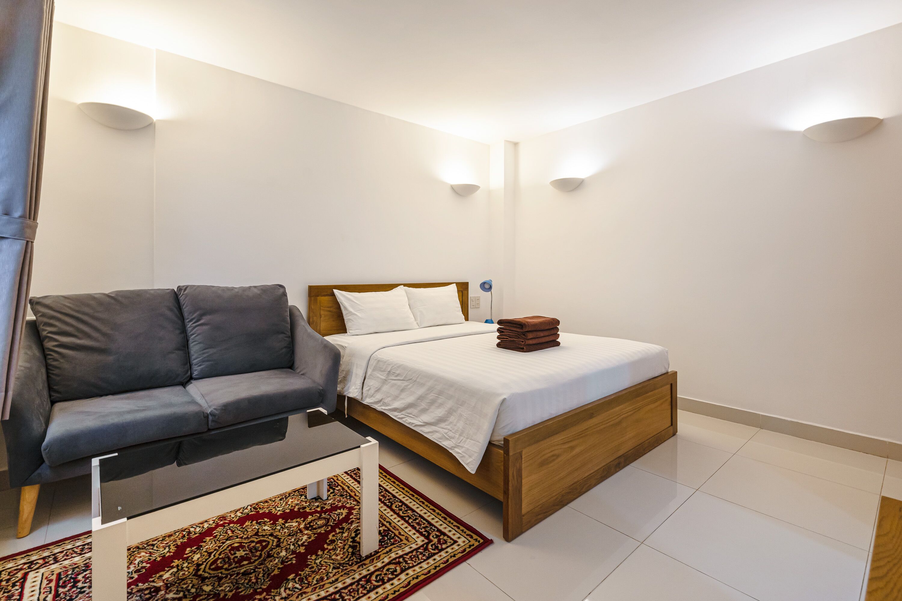 Une chambre à coucher moderne avec un lit, un canapé gris, une petite table et un tapis à motifs.