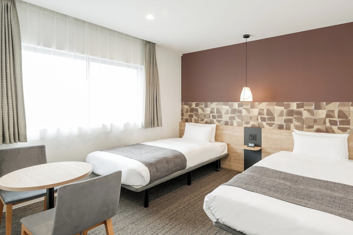 A hotel room with two beds, a small table, and a chair.