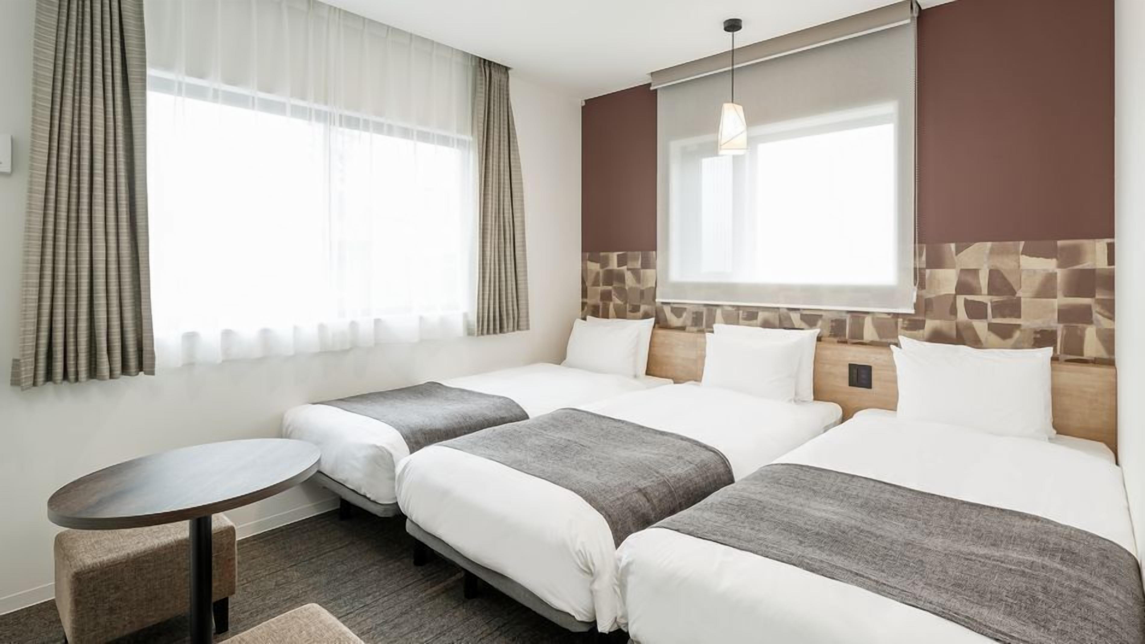A hotel room with two beds, a small round table, and a window with curtains.