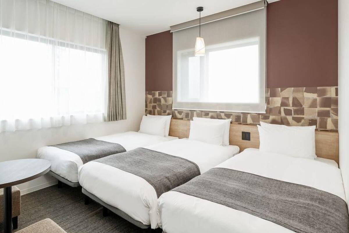 A hotel room with two beds, a small round table, and a window with curtains.