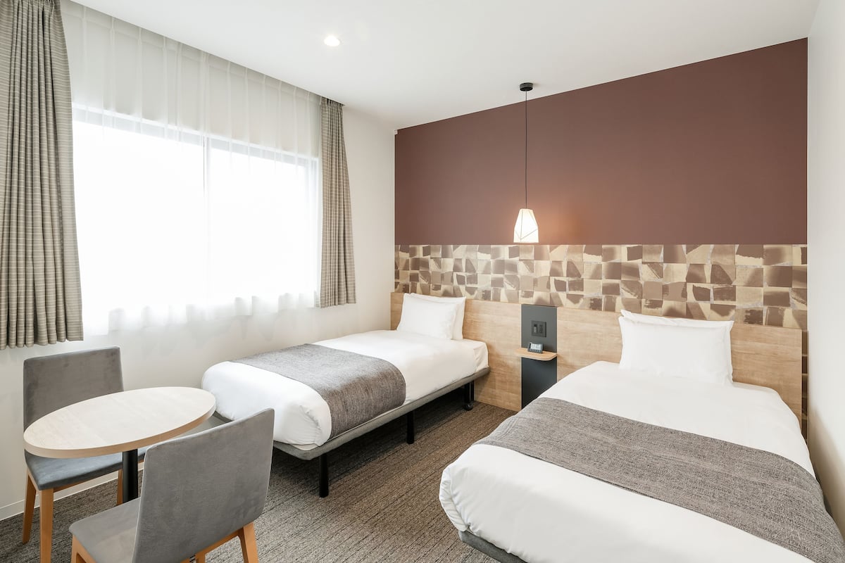 A hotel room with two beds, a small round table, and a chair.