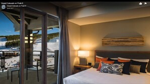 Une chambre d’hôtel avec un lit, une table de chevet, une lampe et une vue sur un paysage enneigé, visible à travers de grandes fenêtres.