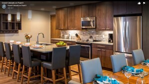 Une cuisine moderne avec des meubles de couleur bois foncé, des appareils en acier inoxydable et un îlot central doté de tabourets de bar.
