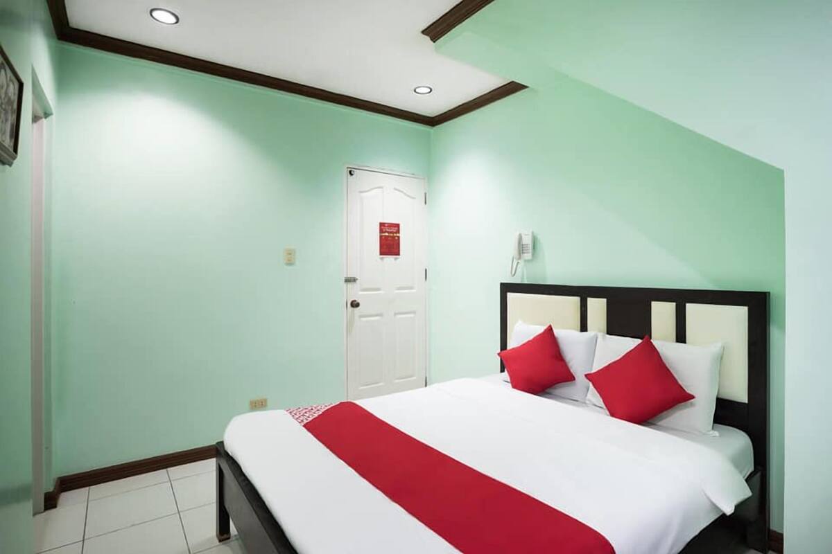 A hotel room with a bed, a door, and a phone on the wall.