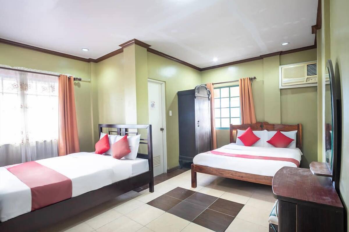A hotel room with two beds, a wardrobe, an air conditioning unit, and a window with curtains.