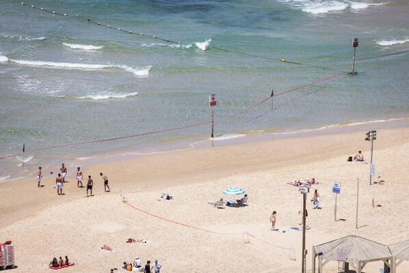 A beach with a volleyball net, umbrellas, and people sunbathing.