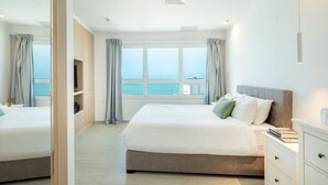 Une chambre d’hôtel moderne avec un grand lit, une table de chevet, une télévision et une vue sur la mer.