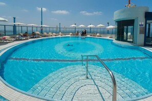 A swimming pool with a clear blue water, a lifeguard stand, and lounge chairs with umbrellas. - Mediterranean Sea Views | 1BR Apt with Balcony (Tel Aviv-Yafo)