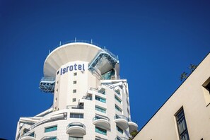 A hotel with a distinctive cylindrical tower, balconies, and a clear blue sky in the background. - Mediterranean Sea Views | 1BR Apt with Balcony (Tel Aviv-Yafo)