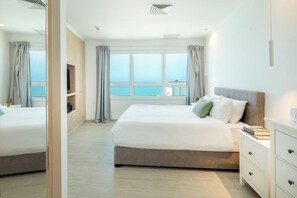 A hotel room with a large bed, a bedside table, a TV, and a view of the sea. - Mediterranean Sea Views | 1BR Apt with Balcony (Tel Aviv-Yafo)
