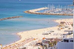 Una playa costera con un puerto deportivo, sombrillas de playa y un faro.