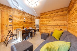 A modern interior with wooden panel walls, a dining area with a table and chairs, and a grey sofa with a yellow pillow.