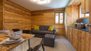 A cozy wooden interior with a dining table set for four, a sofa, and a kitchen area with a countertop. - Marlies Ski in - Ski out 50m, Livigno, Italy (Livigno)
