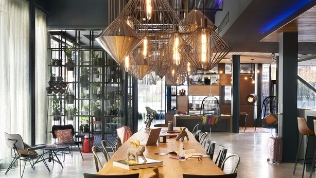 Un vaste espace dédié à la salle à manger, avec une longue table en bois, des chaises modernes et des luminaires suspendus.