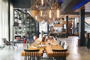 A spacious dining area with a long wooden table, modern chairs, and hanging pendant lights. - Moxy Birmingham NEC and Airport (Birmingham)