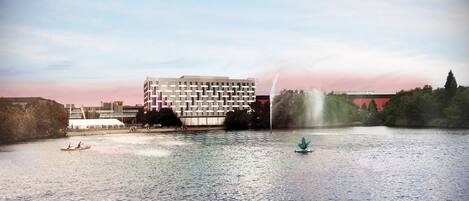 A riverside view with a modern building, a fountain, and a small boat.