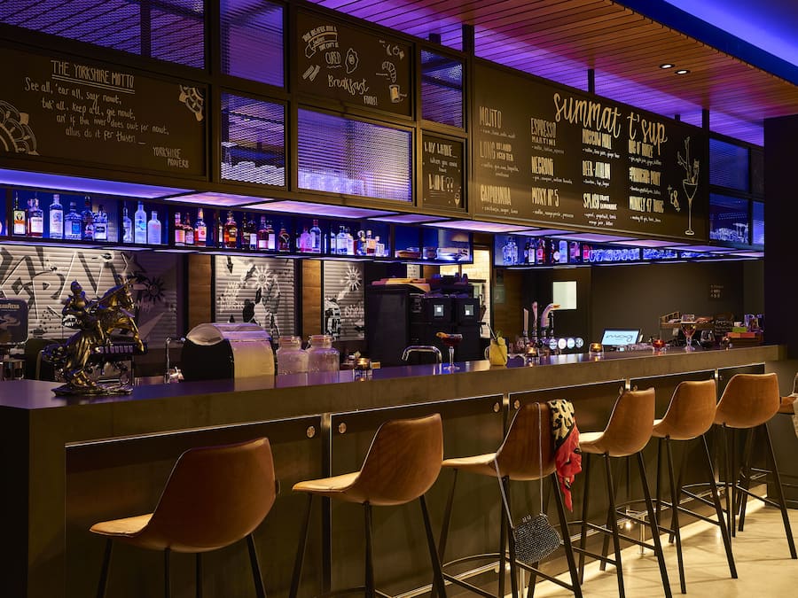 A bar area with a long counter, multiple stools, and a variety of bottles.