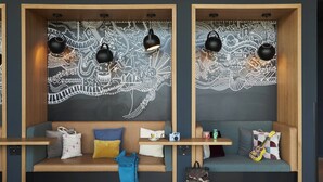 Un intérieur moderne avec deux espaces de détente dotés de structures en bois, chacun agrémenté d’une fresque murale originale, d’une table avec un appareil photo et d’une guitare.