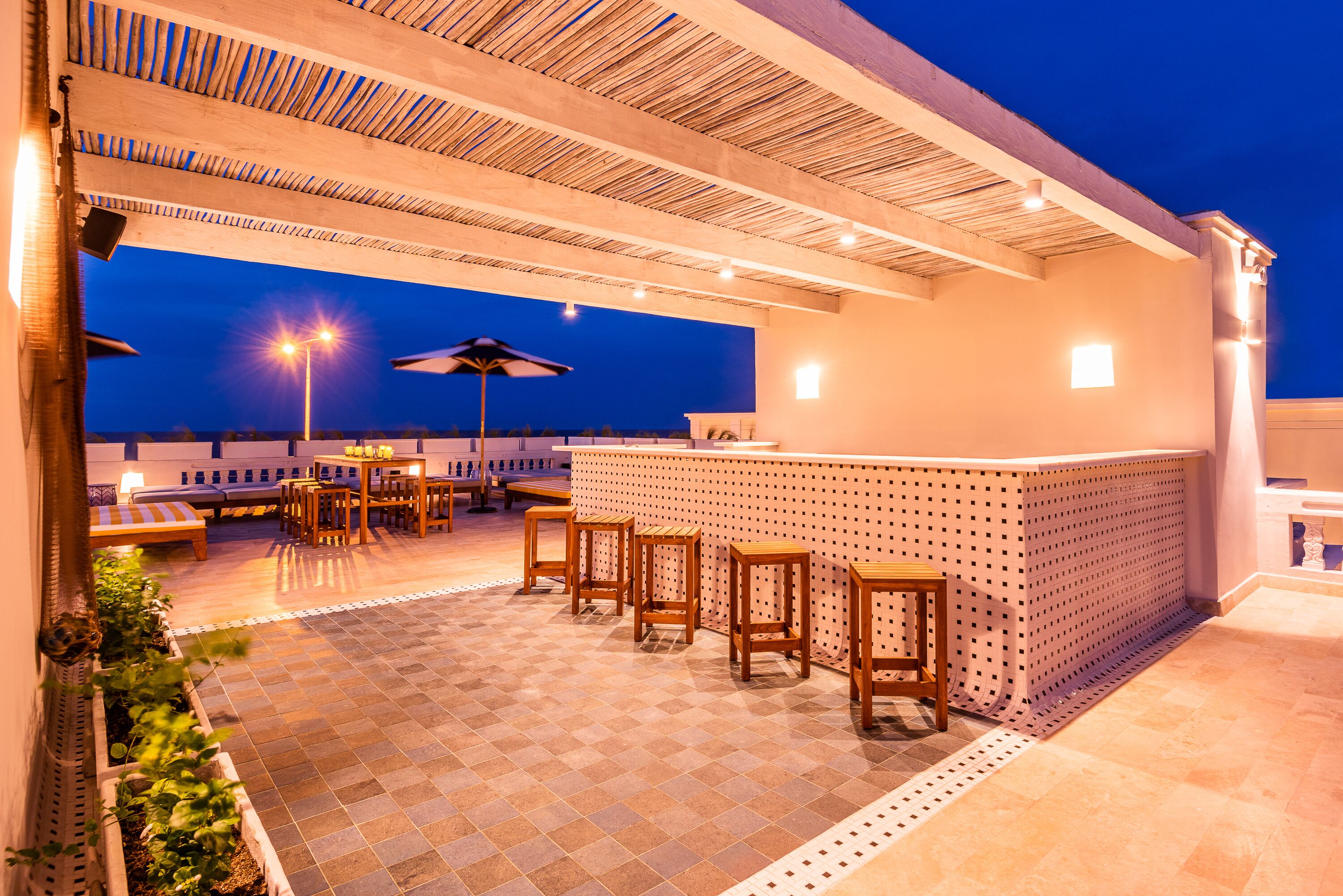 An outdoor patio area with a bar, seating, and a view of the sea at dusk.