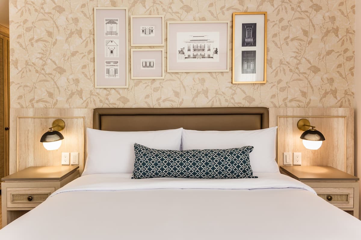 A neatly made bed with a patterned pillow, two bedside lamps, and framed architectural drawings on the wall.
