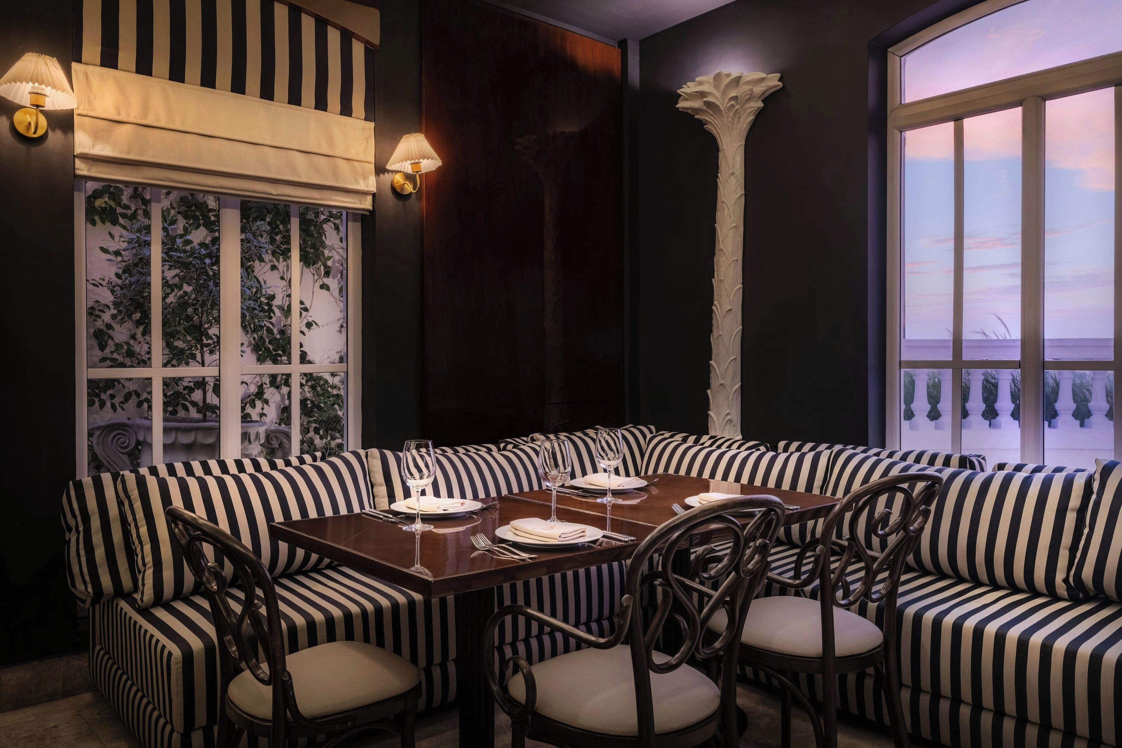 A dining area with a dark wood table, striped upholstered seating, and a view of the sky through a window.