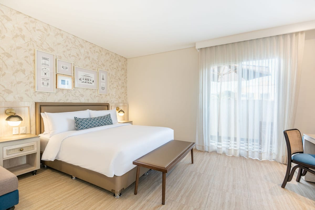 A hotel room with a large bed, bedside tables with lamps, a desk, and a chair.