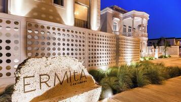Un segnale di pietra con l'incisione 'ERMITA CARTAGENA', un edificio con un balcone e un ingresso ben illuminato.