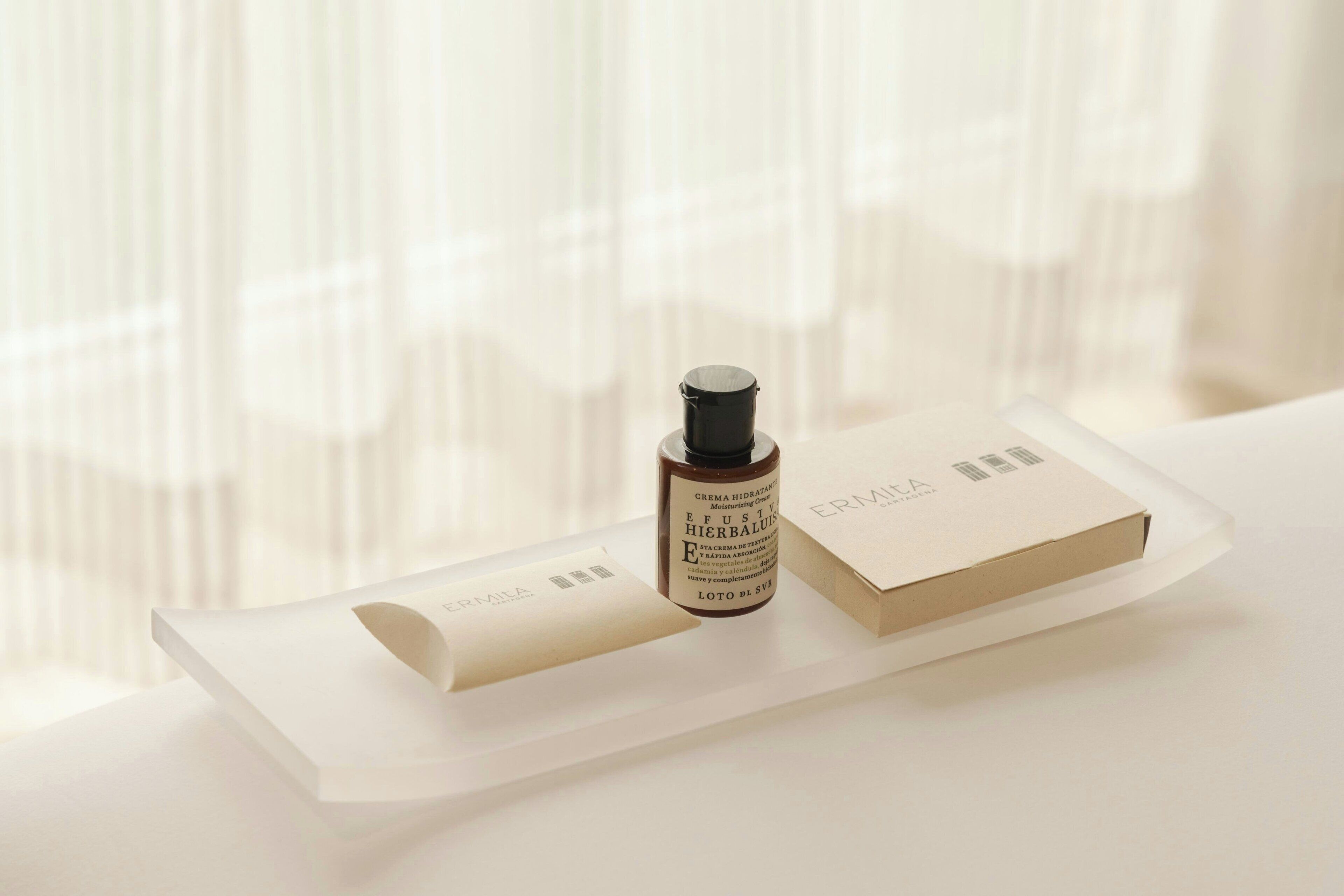 A bottle of skincare product and a box on a white surface with a window in the background.