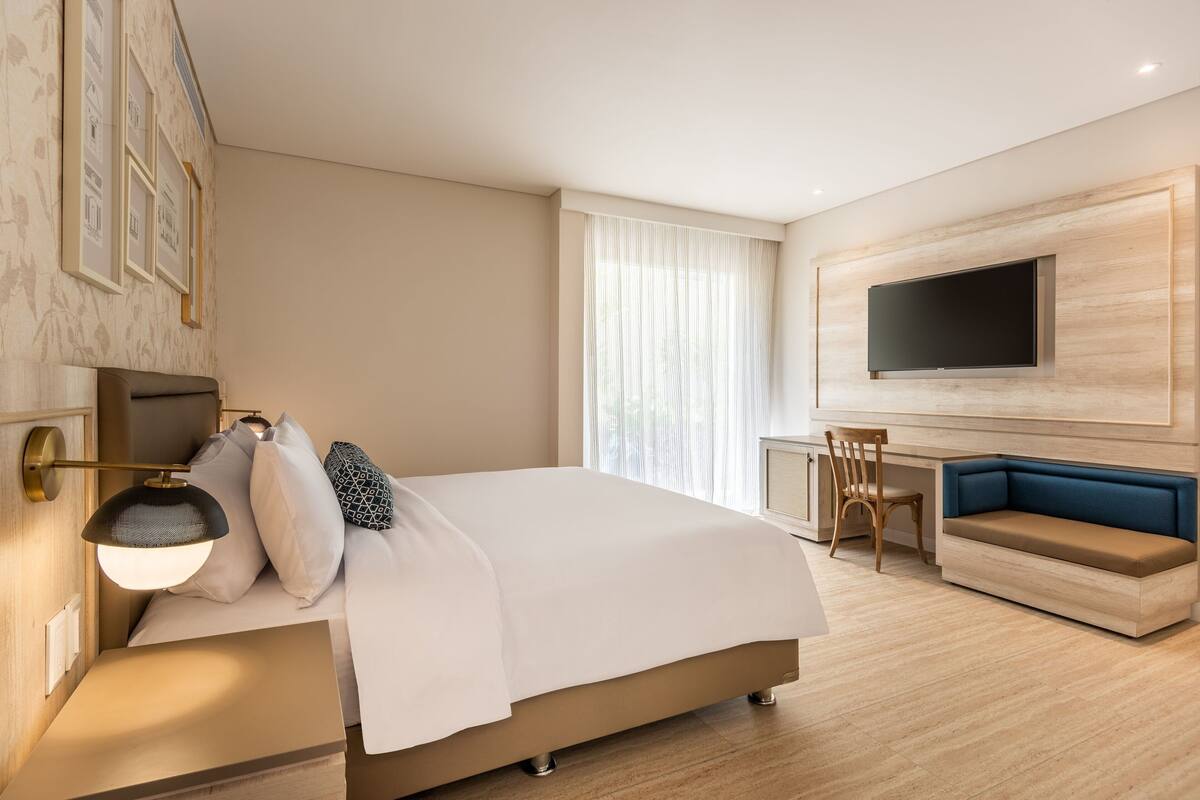 A modern hotel room with a large bed, a desk, a blue sofa, and a TV mounted on the wall.