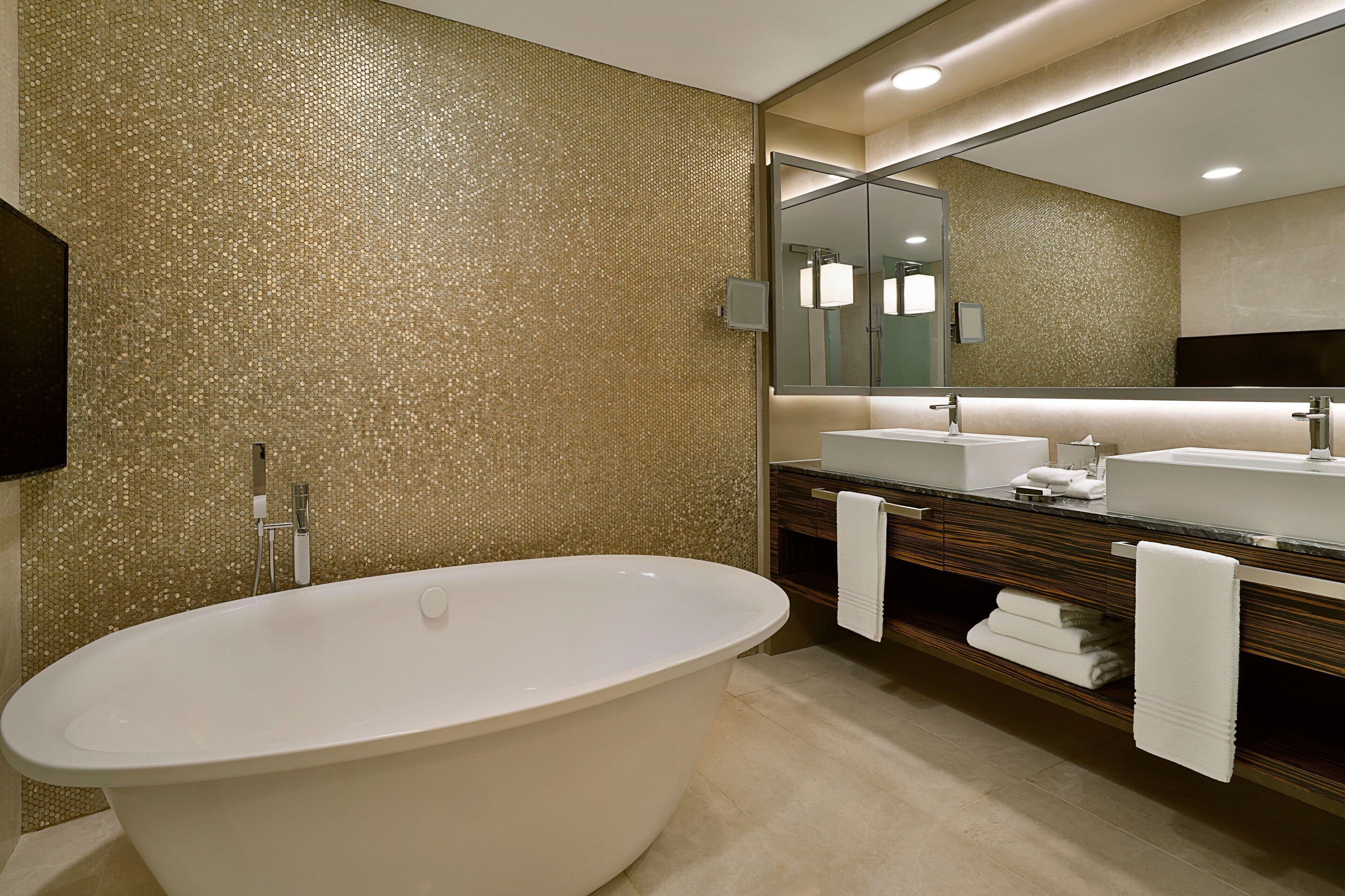 A modern bathroom with a freestanding bathtub, a large mirror, and a vanity with a sink and towel rack.