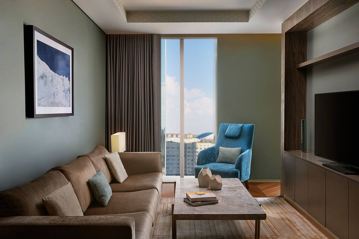 A modern living room with a brown sofa, a blue armchair, a coffee table, and a large window with a view of buildings.