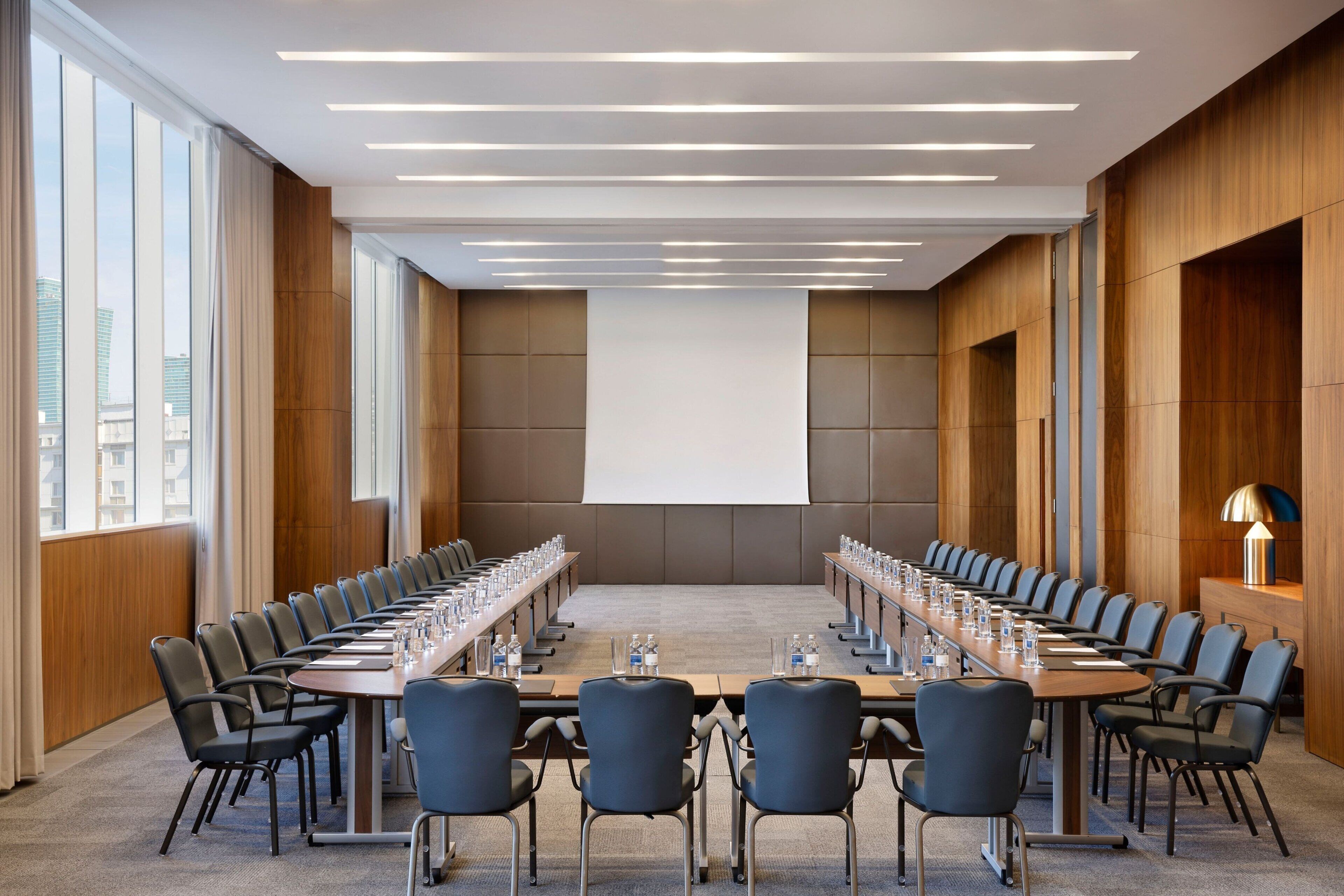 A conference room with a long table, chairs, a projector screen, and a wooden wall panel.