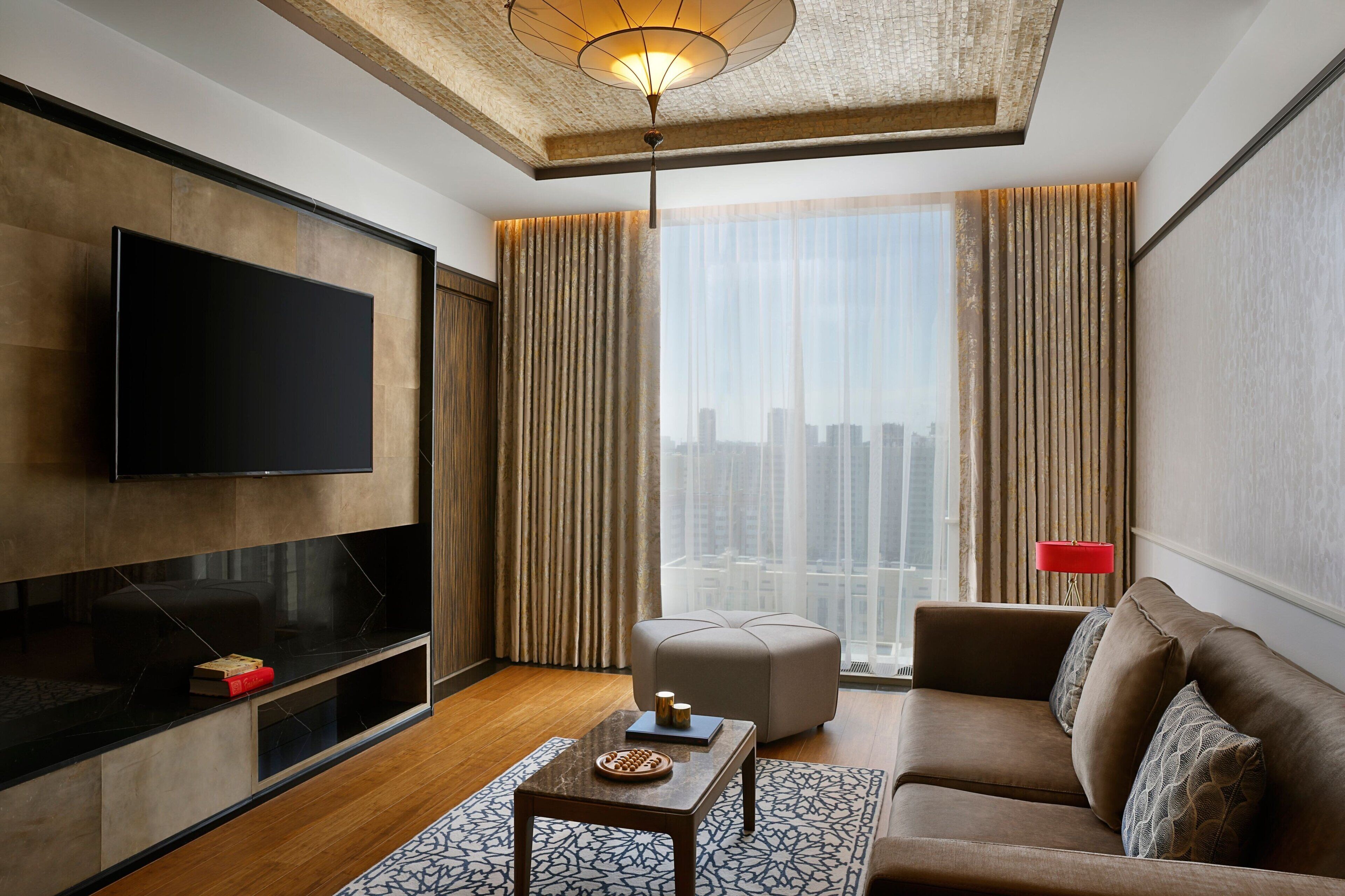 Una sala de estar moderna con un televisor de pantalla plana, un sofá, una mesa de centro y vistas a la ciudad a través de ventanas amplias.