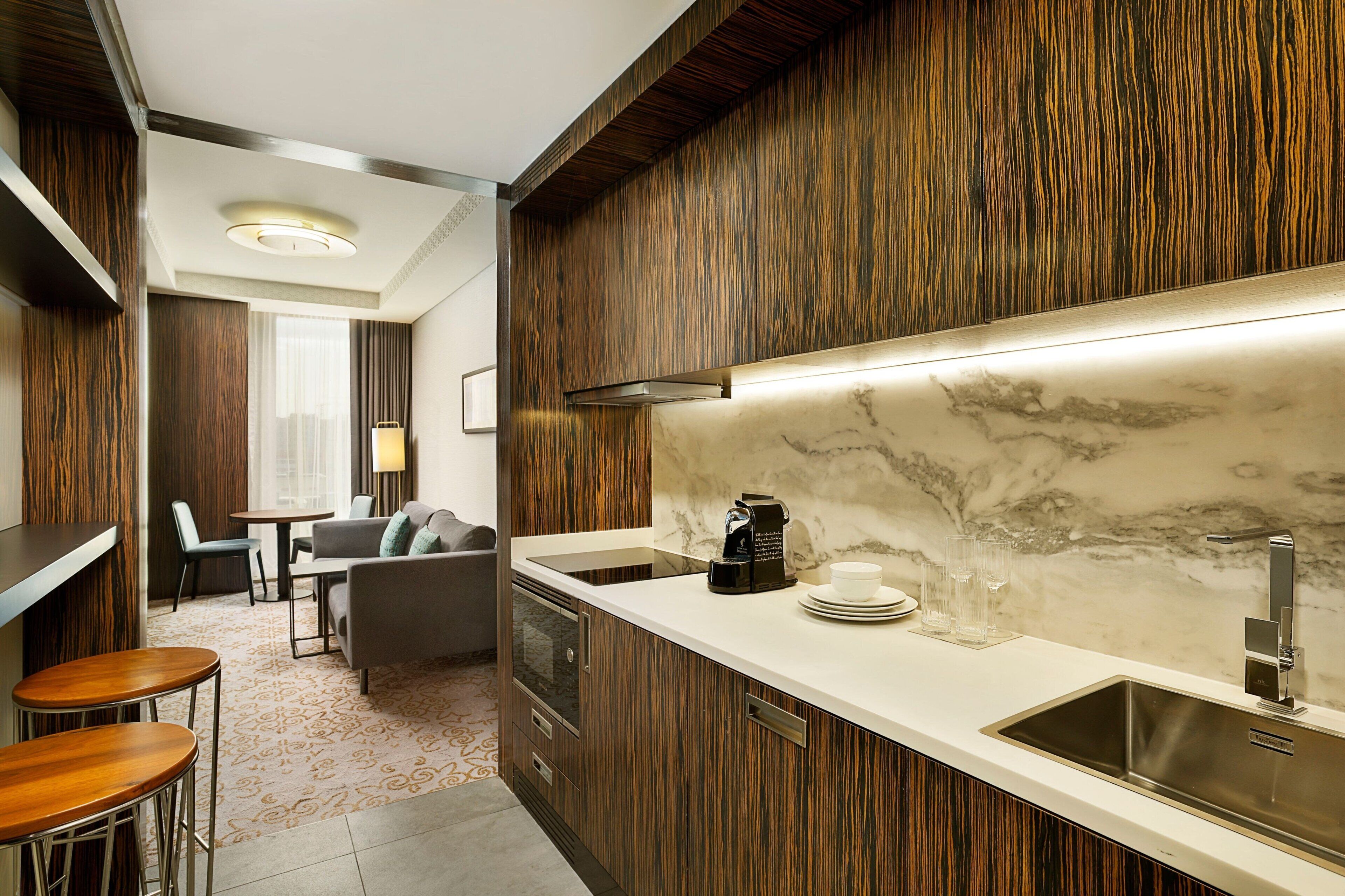 A modern kitchen with a marble countertop, wooden cabinetry, and a built-in stove.