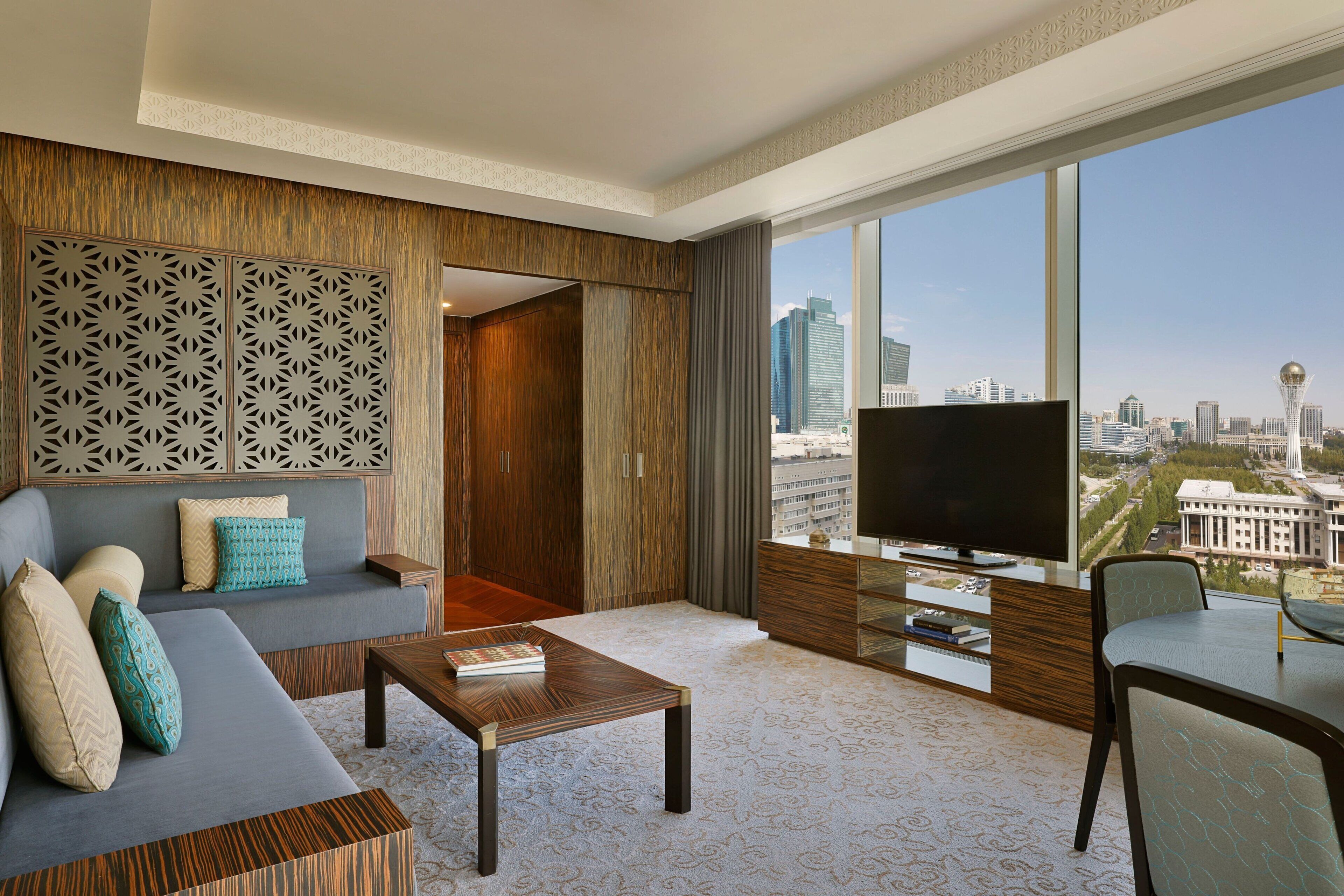 A modern hotel room with a large window, a sofa, a coffee table, and a TV.