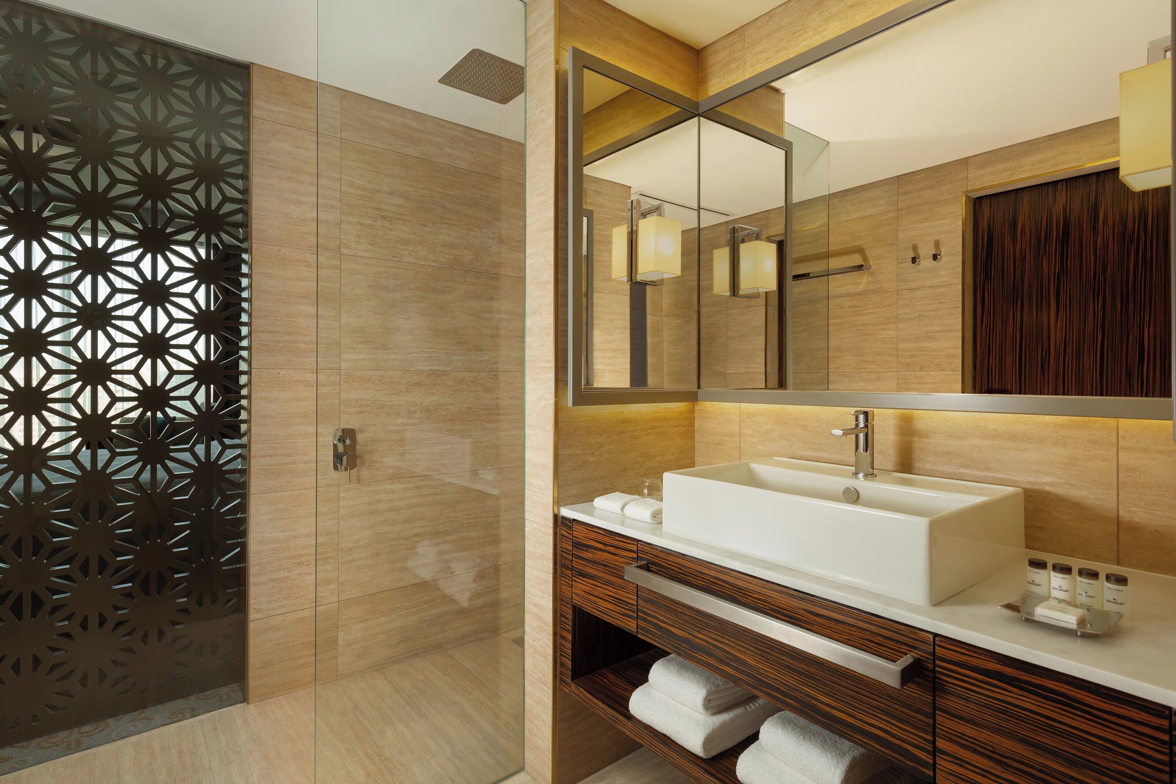 A modern bathroom with a large mirror, a white sink, and wooden cabinetry.