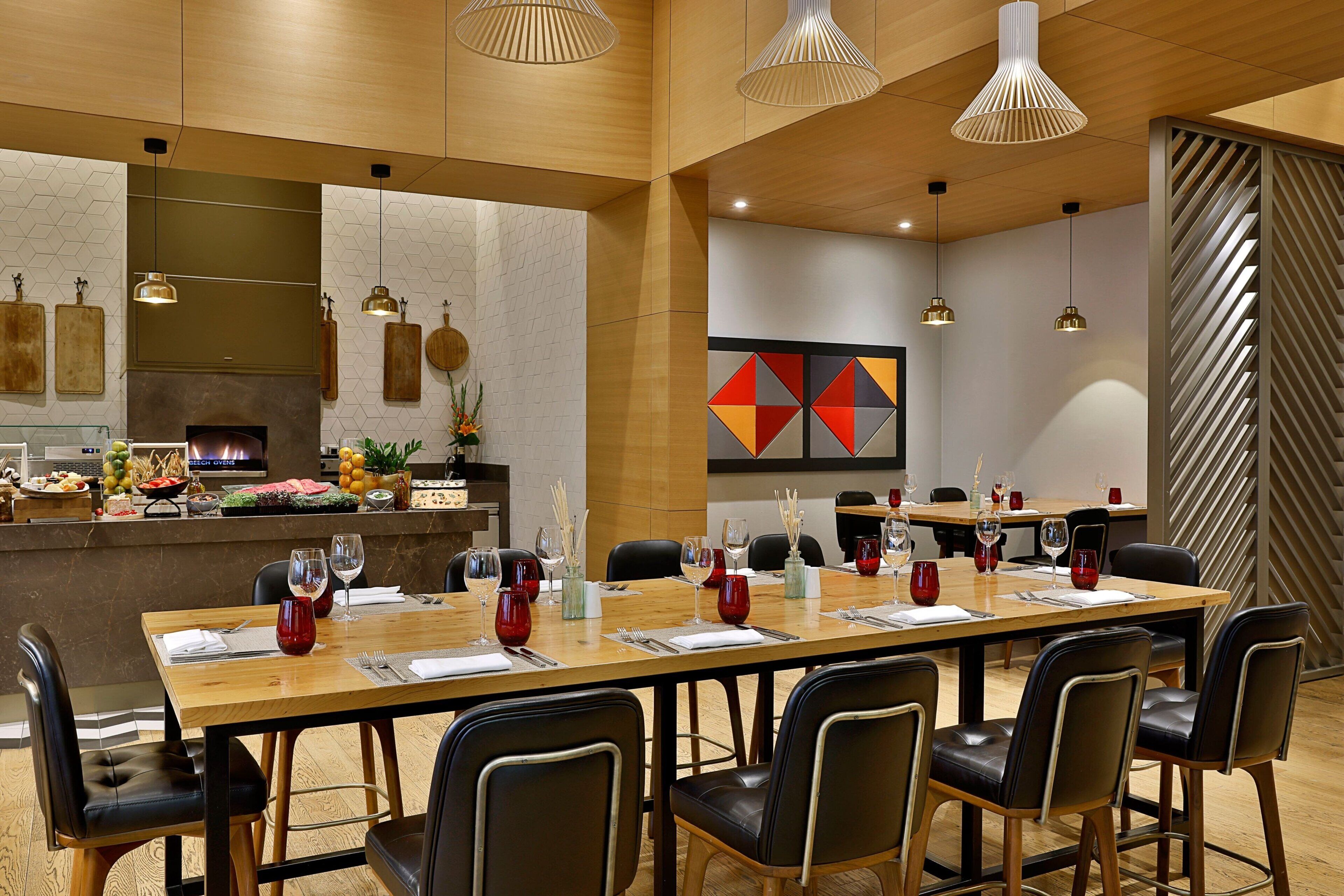A modern dining area with a long wooden table set for a meal, surrounded by black chairs.