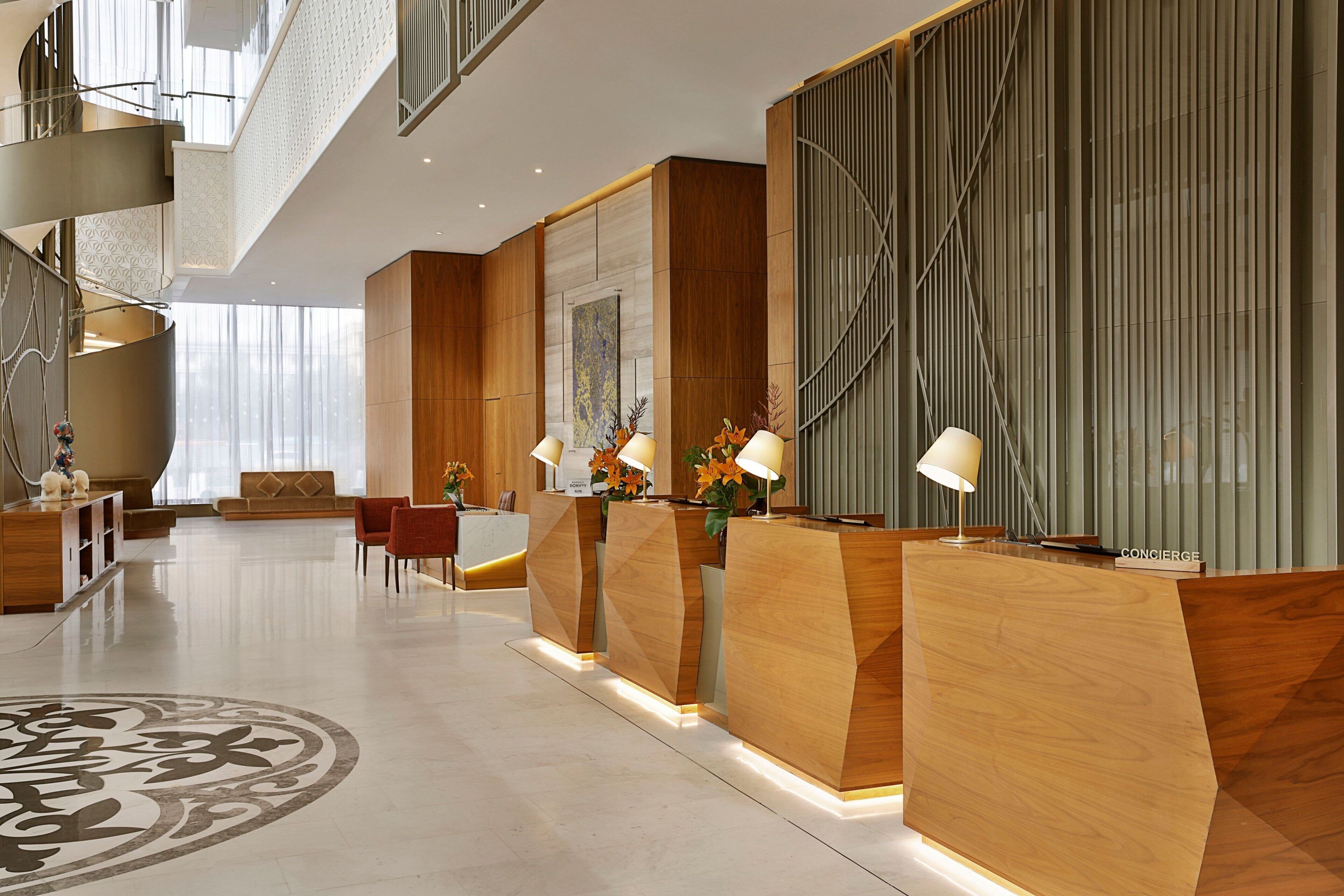 Un moderno vestíbulo de hotel con una recepción central, área de descanso y un diseño decorativo en el suelo.
