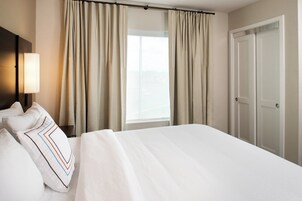 A hotel room with a large bed, beige curtains, a window, and a door.