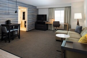A hotel room with a dining area, a TV, a sofa, and a lamp.
