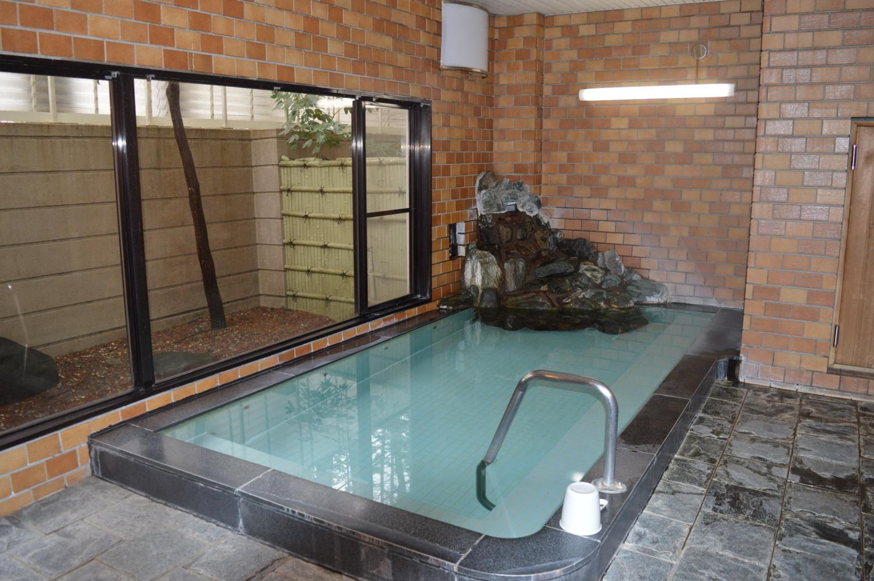 A swimming pool with a glass enclosure, a stone wall, and a wooden door.
